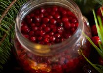 Cranberries in a large jar with fruit juice soaking up the sugar