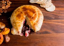 A large wheel of cheese wrapped in puff pastry filled with cranberry holiday sauce.