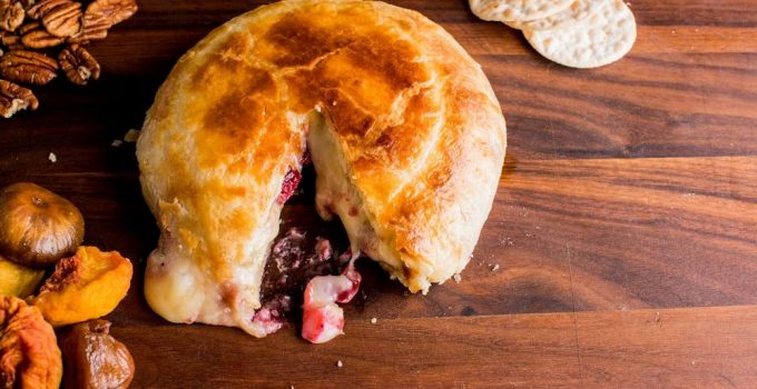 A large wheel of cheese wrapped in puff pastry filled with cranberry holiday sauce.