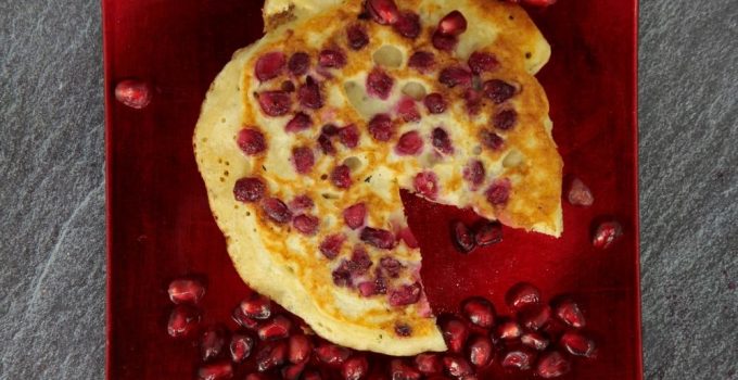A round pancake on a red plate with berries all around.